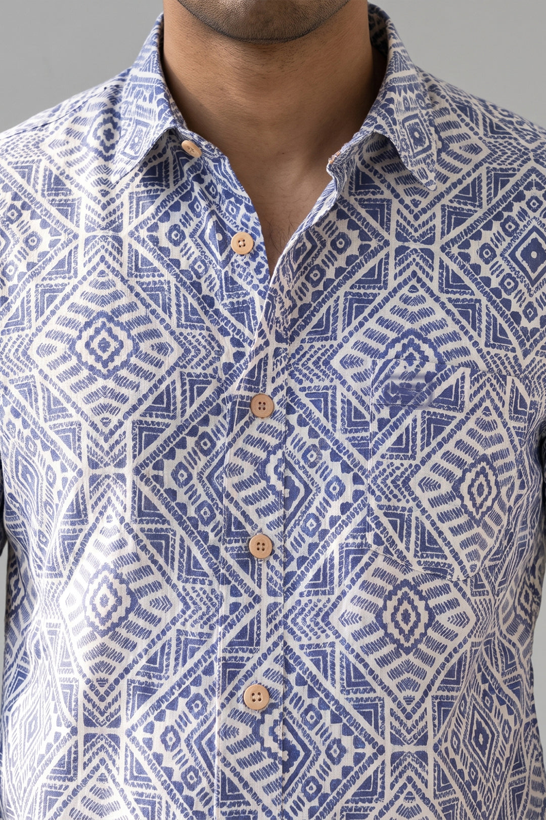 A close-up of a man wearing a blue and white geometric patterned button-down shirt with wooden buttons.
