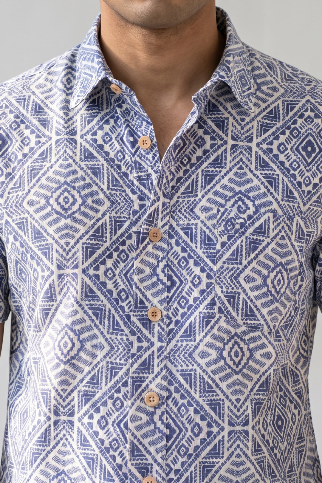 A close-up of a man wearing a short-sleeve button-up shirt with a blue and white geometric block print pattern and light brown buttons.