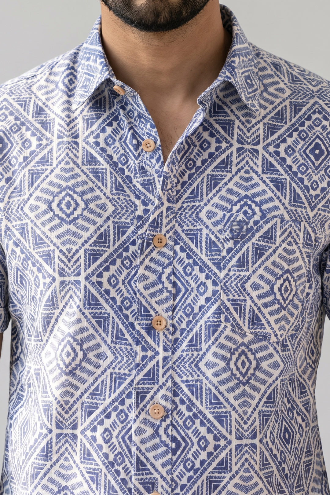 A close-up of a man wearing a blue and white geometric patterned button-down shirt, showing the collar, front buttons, and pattern details.