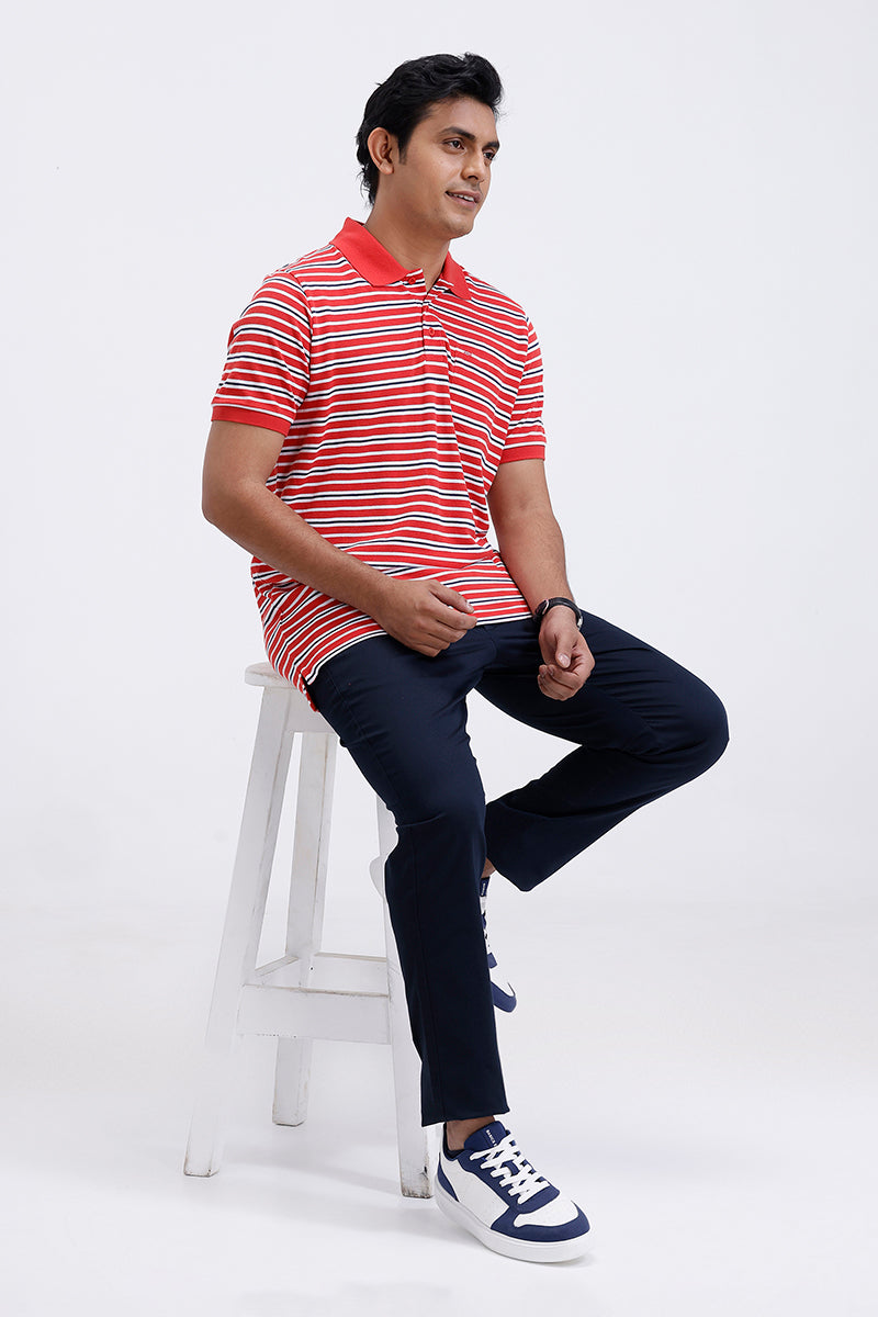 Man sitting on a stool wearing a red and white striped polo shirt and dark jeans.