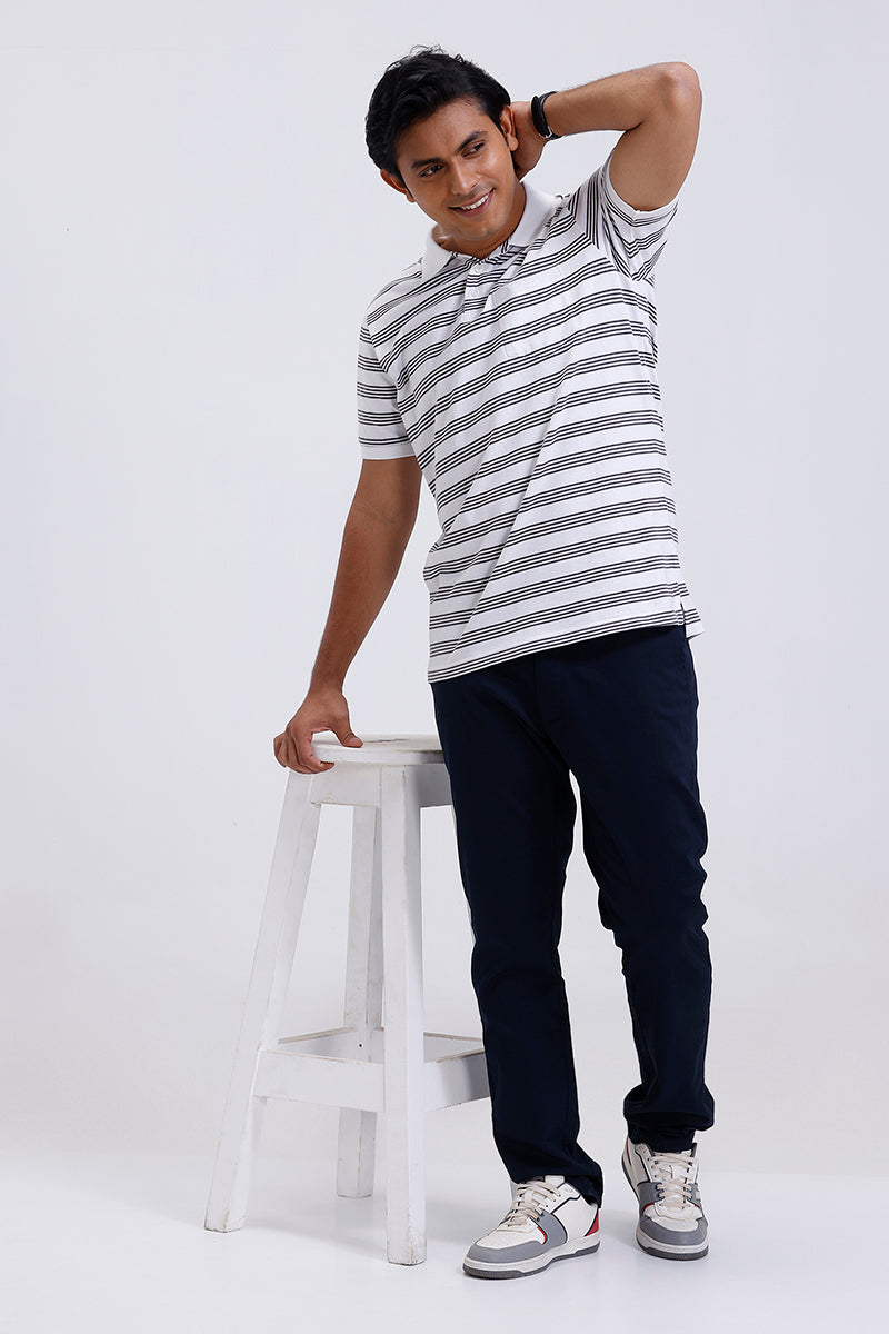 Man wearing a striped t-shirt and dark pants standing on a white stool against a white background